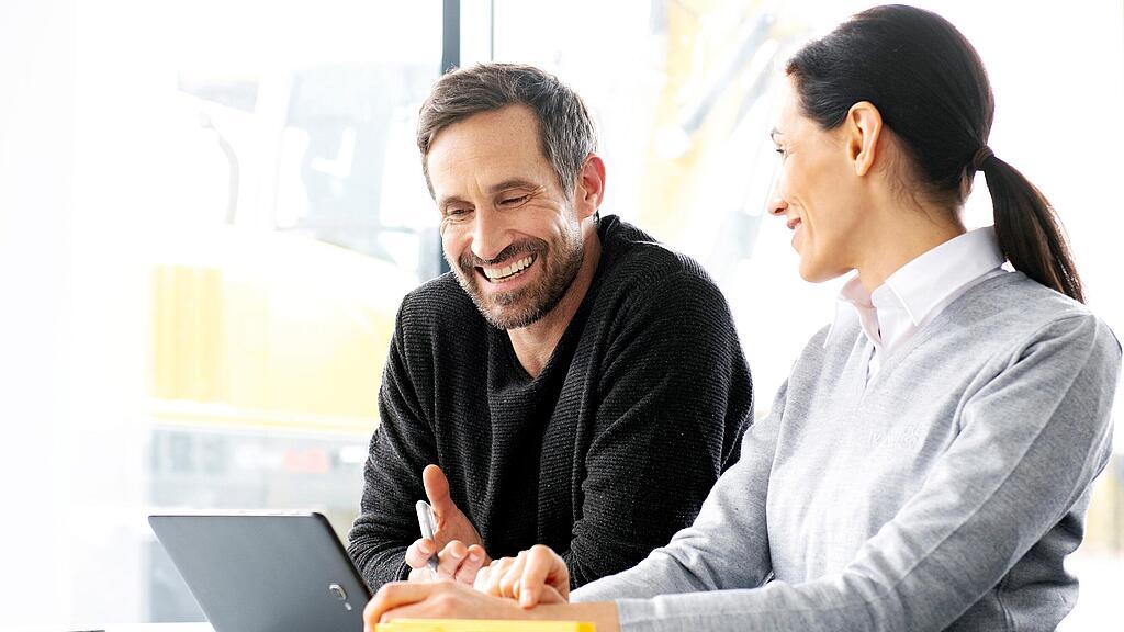 Kunde sitzt mit Wacker Neuson Verkäuferin vor Laptop und wird zu gebrauchten Baumaschinen und Baugeräten beraten.