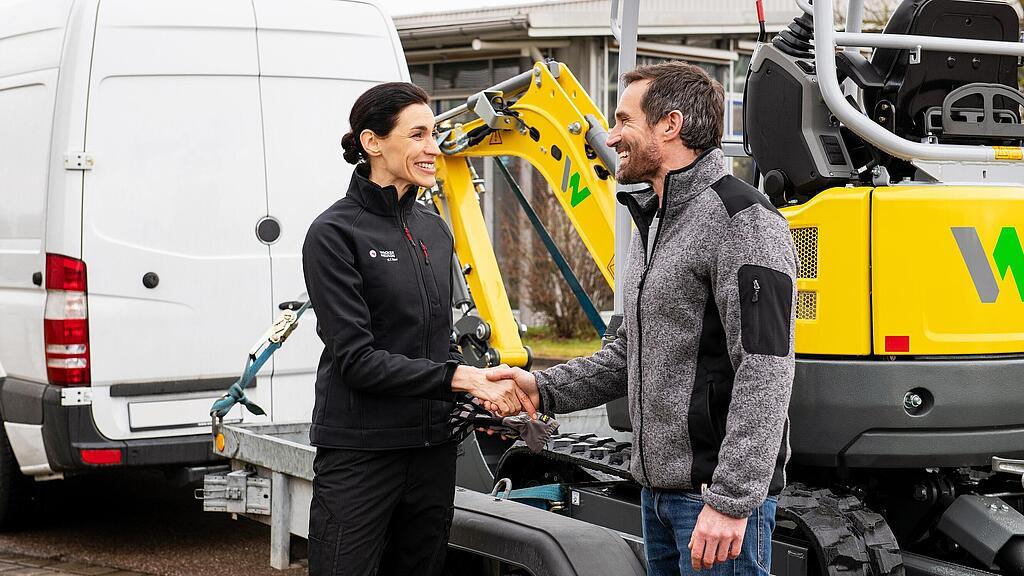Wacker Neuson Mitarbeiterin gibt Kunden die Hand vor einem Wacker Neuson zero emission Kettenbagger.