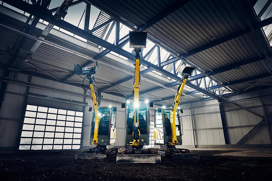 Drei Wacker Neuson Minibagger mit angehobenen Auslegern in Industriehalle