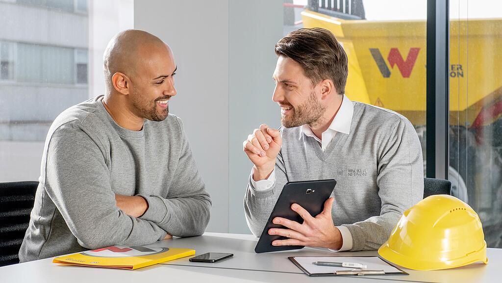 Wacker Neuson employee sitting at a desk and showing customer something on a tablet.
