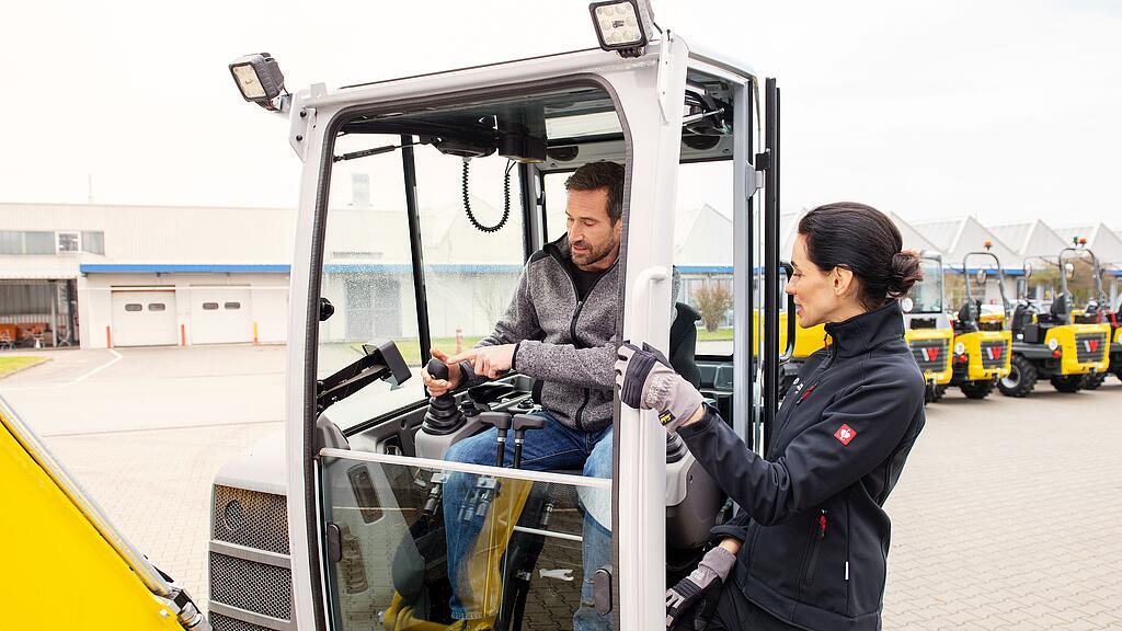 Ein Mitarbeiter von Wacker Neuson berät einen Kunden, der in einem Wacker Neuson-Kettenbagger sitzt, über das klassische Angebot für die Miete von Wacker Neuson.