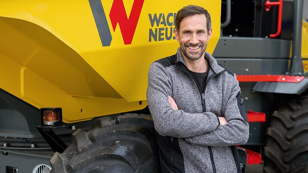 Wacker Neuson Kunde steht lächelnd mit verschränkten Armen vor einem Wacker Neuson Raddumper.