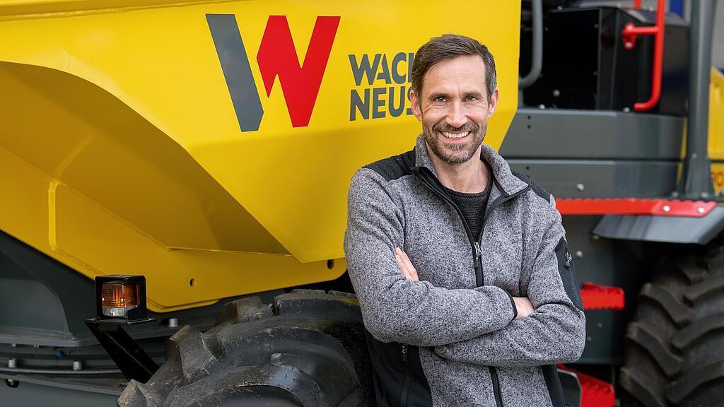 Wacker Neuson Kunde steht lächelnd mit verschränkten Armen vor einem Wacker Neuson Raddumper.