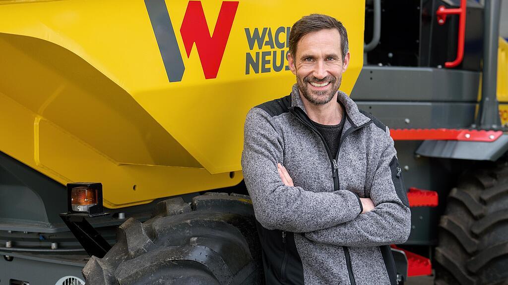 Wacker Neuson Kunde steht lächelnd mit verschränkten Armen vor einem Wacker Neuson Raddumper.