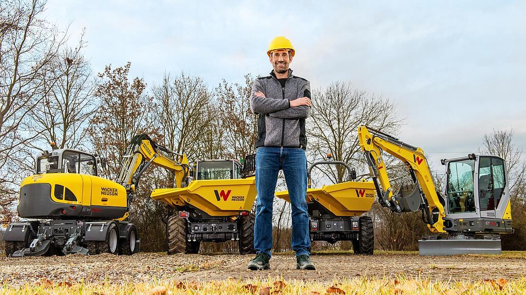 Wacker Neuson Kunde steht lächelnd mit verschränkten Armen vor einem Wacker Neuson Mietpark.